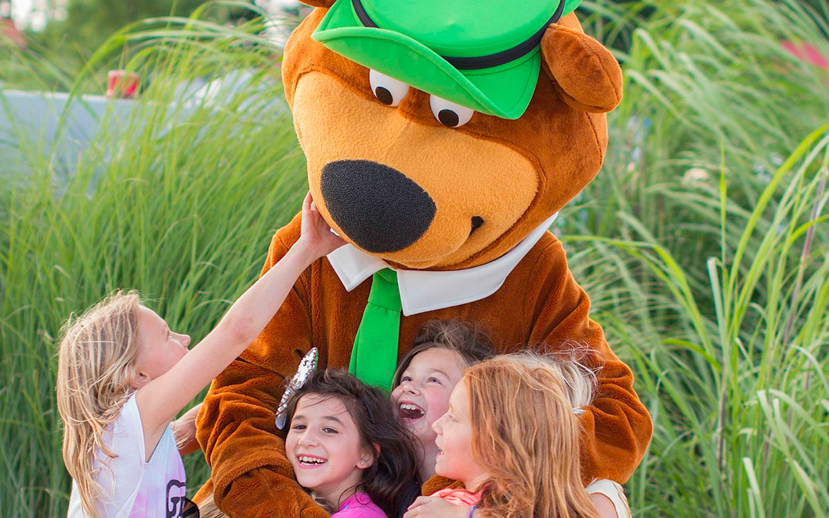 Four children playing with Yogi Bear in tall grass