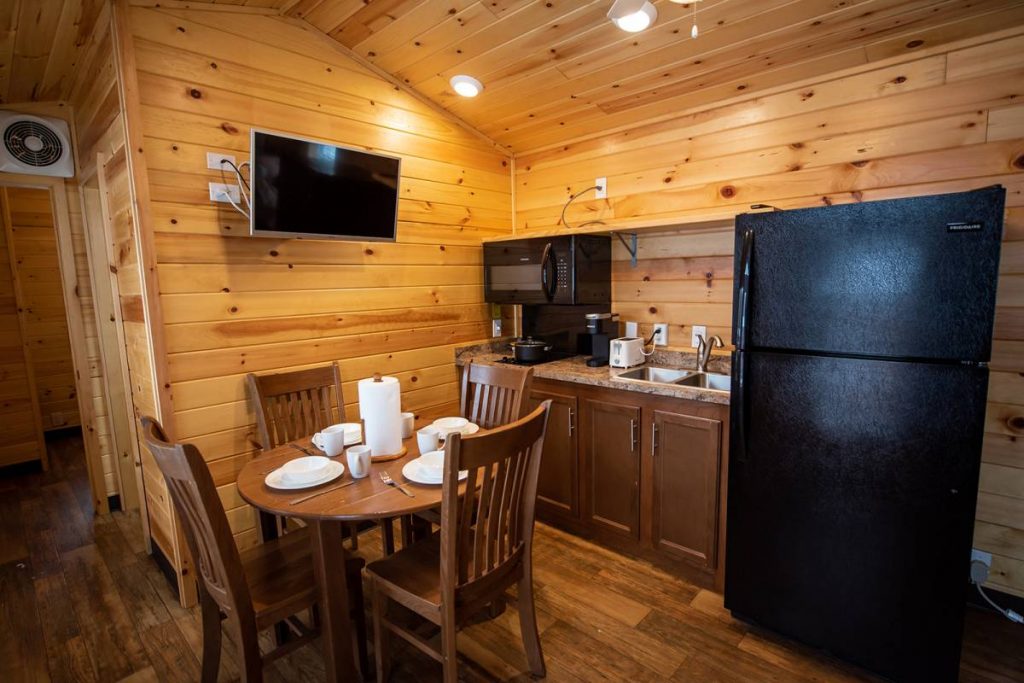 Yogi Bear Cabin Interior, Kitchen with refrigerator, sink and microwave, dining table and dishes, and TV