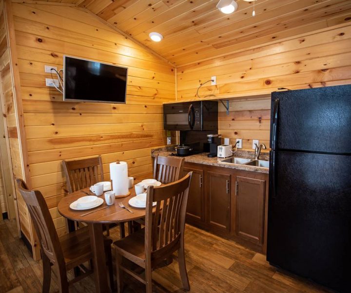 Yogi Bear Cabin Interior, Kitchen with refrigerator, sink and microwave, dining table and dishes, and TV