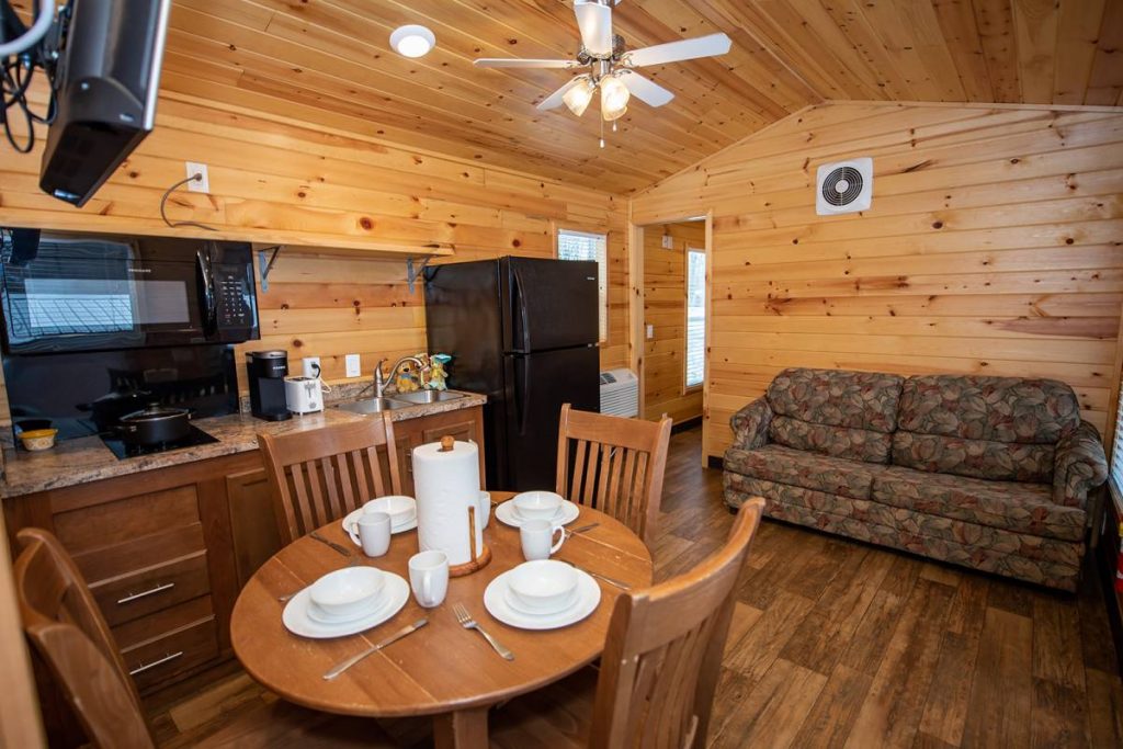 Yogi Bear Cabin Interior, Kitchen and Living space with couch, dining table with dishes, microwave, sink, and ceiling fan