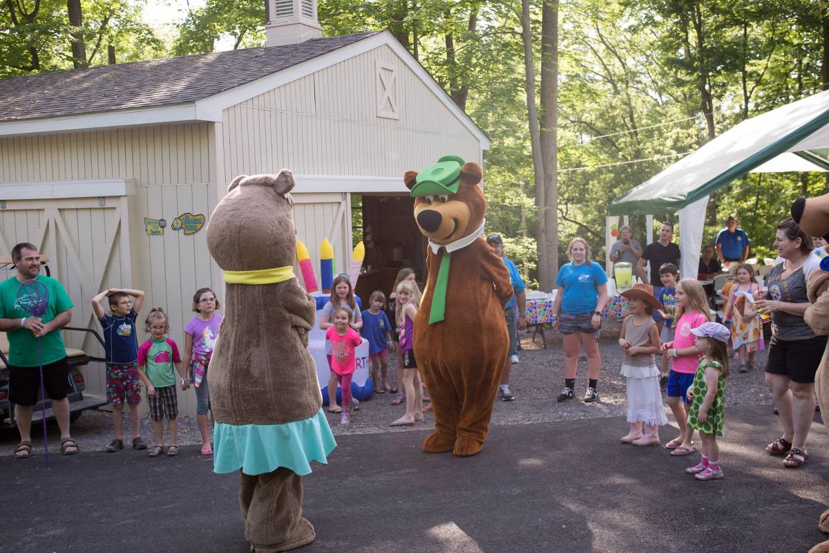 Two bear mascots appear to discuss with each other with an audience of children and adult campers