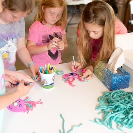 Kids working on arts and crafts involving yarn, markers, googley eyes, and foam