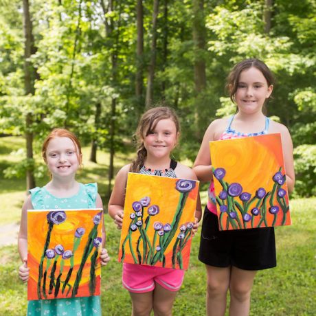 Three children proudly display their painting projects