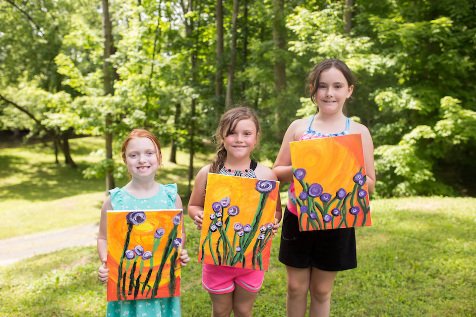 Three children proudly display their painting projects