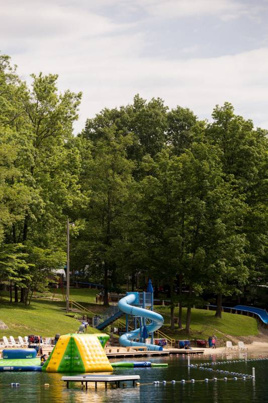 Distant shot of tall trees, water park, enclosed lake area, and floating inflatable playstructure