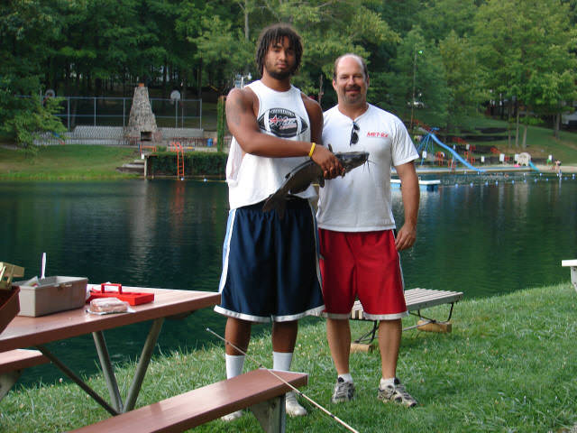 Two men with fishing gear holding a catfish and posing for the camera