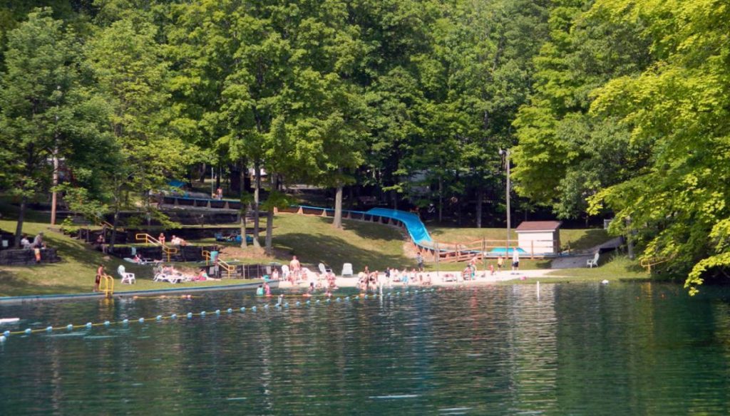 Lake and beach with many campers, waterslide, and enclosed lake area