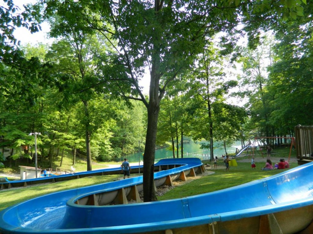 Large plastic water slide winding through the grassy forest with a swingset and slide visible