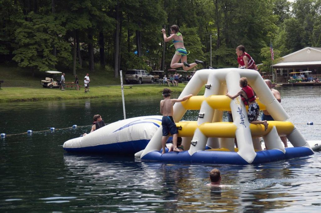 Several children climbing a large inflatable structure floating in the lake, one leaping off the float