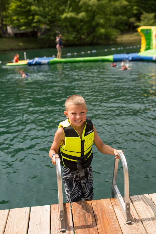 Happy child exiting the lake on a ladder, wearing a flotation vest