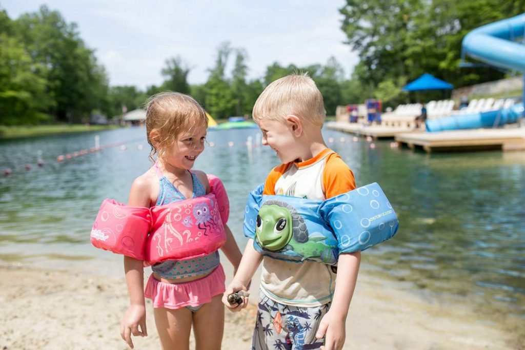 Two young children on the beach smiling at each other with flotation devices