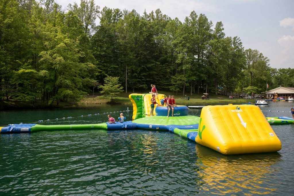Children playing on a large floating structure in the lake, wearing flotation devices