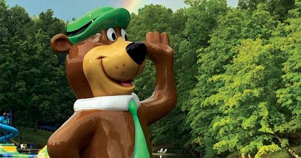 statue of yogi bear waving with a rainbow behind him